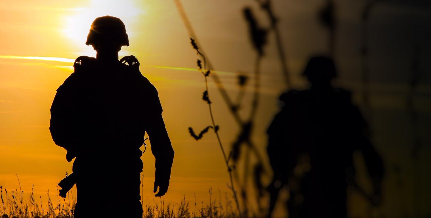 Silhouettes of the back of two soldiers in a field at dusk